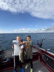 Two young anglers holding a trophy lake trout aboard a Lake Michigan fishing charter near Whitehall, Michigan.