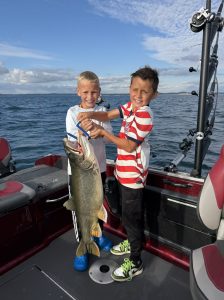 Two young anglers holding a trophy lake trout aboard a fishing charter boat near Whitehall, Michigan.
