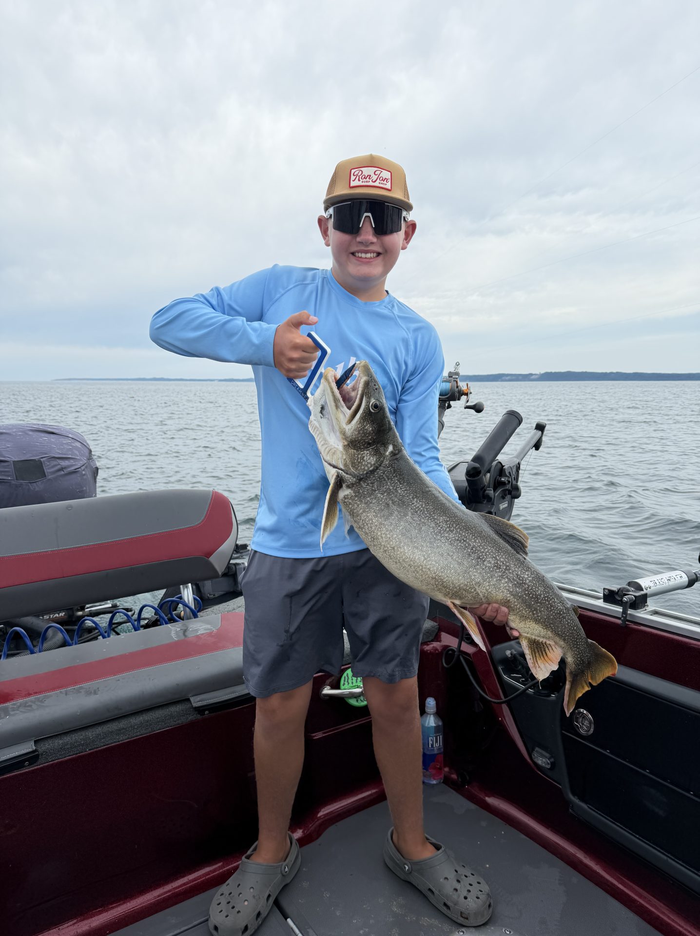 Young angler holding a large lake trout aboard a fishing boat on White Lake near Whitehall, Michigan during a summer fishing trip.