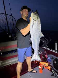 Angler holding a giant king salmon aboard a fishing boat during an early morning Lake Michigan salmon charter near Whitehall, Michigan.